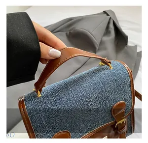 Detail of blue denim handbag featuring brown leather handle and gold metal hardware