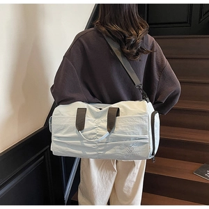 Detailed back view of a beige large travel duffel bag on indoor stairs with shoulder strap