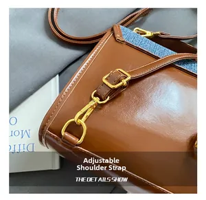 Detail of brown leather and blue denim stitching with adjustable strap and gold buckle