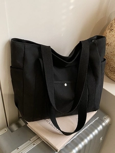 Minimalistische schwarze Canvas-Tragetasche mit Seitentaschen auf einem grauen Koffer