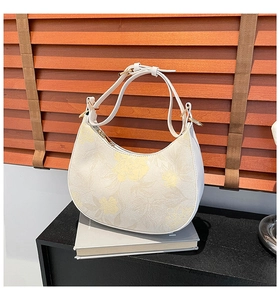 Detailed view of white hobo bag with yellow floral print and gold hardware on a book