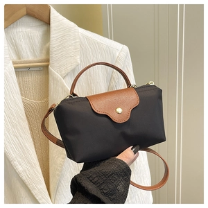 Close-up of a mini black nylon crossbody bag with brown leather flap and gold hardware