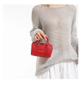 Gros plan du mini sac Boston rouge en cuir grainé porté par un mannequin en tenue chic