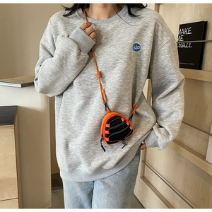 Close-up of a mini orange triangular crossbody neck pouch worn over a grey sweatshirt