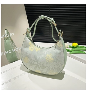 Detail of light green crescent bag with floral patterns and golden hardware