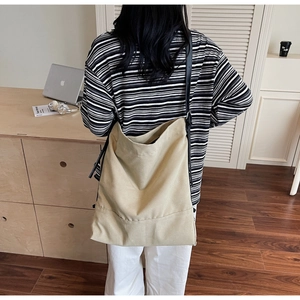 Große beige Canvas-Einkaufstasche mit schwarzen Lederriemen am Modell in einer Büroumgebung