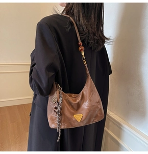 Detail of a brown leather hobo bag featuring amber beads and a triangle logo