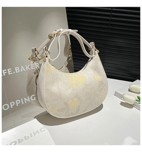 Detail of crescent bag featuring floral pattern, gold hardware and smooth zipper closure
