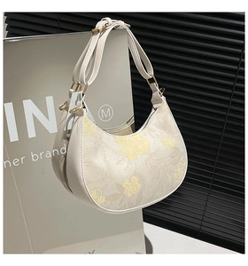 Detail of floral beige crescent bag with gold hardware on a minimalist metal display
