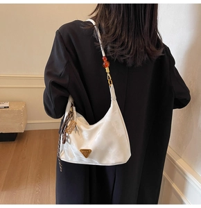 Detail of white half-moon bag with triangle metal logo and amber bead on the strap