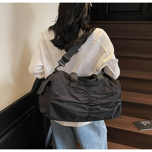 Detailed view of the black pleated nylon travel bag worn by a model on stairs