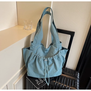 Light blue nylon tote bag with front drawstring pocket placed on black luggage