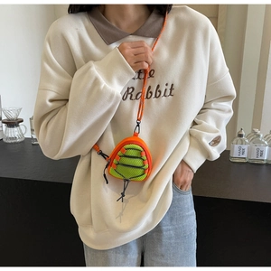 Close-up of bright orange and green mesh mini purse worn with cream white sweatshirt