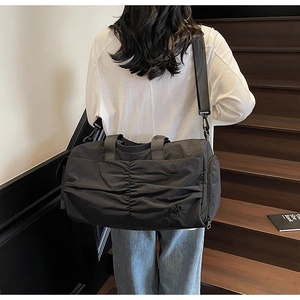 Fashionable black nylon travel bag with pleated design worn on shoulder by a model