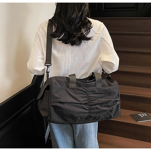 Detail of black pleated travel bag showing reinforced handles and adjustable strap