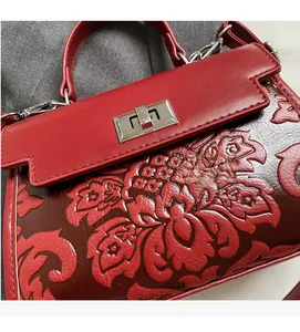 Close-up of red leather handbag showing floral embossed pattern and silver metal twist lock