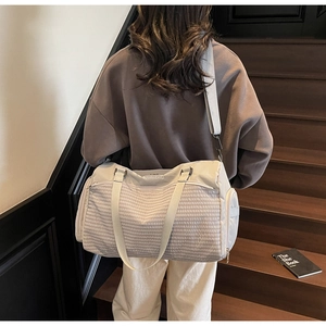 Frau trägt große beige Fitness-Reisetasche mit Streifenmuster auf hölzerner Innentreppe