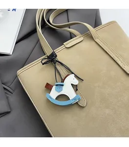 Close-up of a white rocking horse leather bag charm attached to a brown tote bag handle