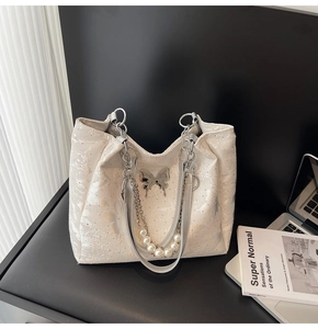 Détail du sac cabas argenté avec charm papillon en métal et chaîne décorative en perles