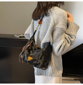 Detail of a black textured hobo bag featuring a gold triangle logo and amber bead strap