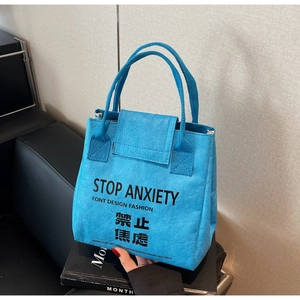 Detail of blue Tyvek tote bag featuring bold Stop Anxiety text on a textured surface