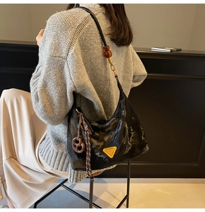 Detail of black glossy shoulder bag with amber bead strap and pretzel charm accessory