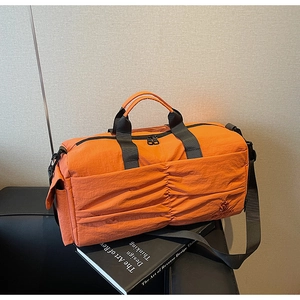 Detail of orange nylon travel bag with crossbody strap on aesthetic book background