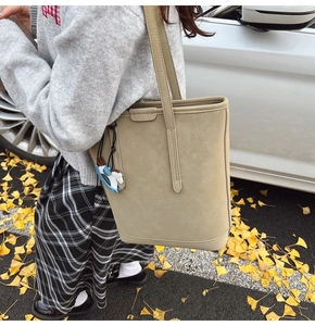 Chic khaki-grey textured bucket bag with blue horse charm shown in street style scene