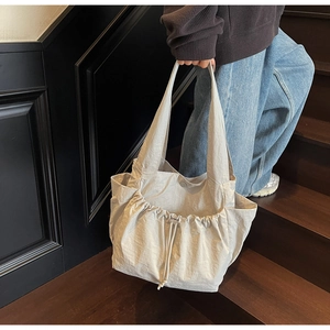 Detail of a large beige tote bag with drawstring closure and practical side pockets