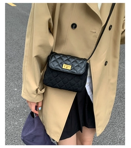 Detail of a quilted crossbody bag with gold lock on a trench coat street style