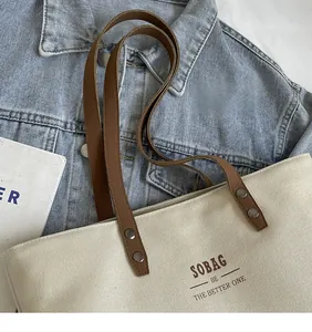 Detail of off-white canvas tote with brown leather strap and SOBAG lettering