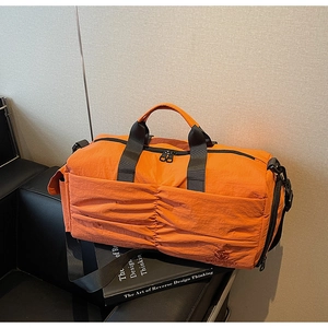 Orange nylon travel bag with side pleats and adjustable strap on a leather bench