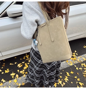 Chic beige suede bucket bag with blue horse charm shown in a seasonal autumn street setting