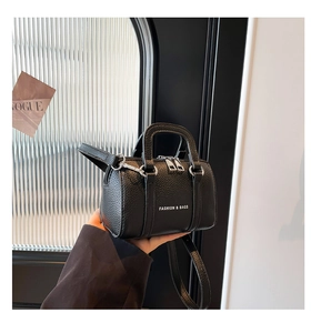 Gros plan d'un mini sac Boston noir en cuir grainé avec doubles poignées et bandoulière