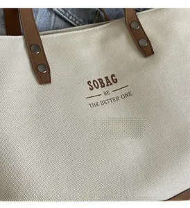 Close-up of cream canvas tote bag with brown leather handles and metal rivet details