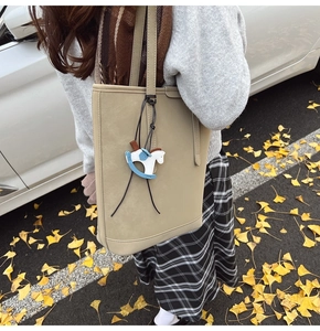 Detail of beige textured leather tote bag with a blue horse charm in an outdoor setting