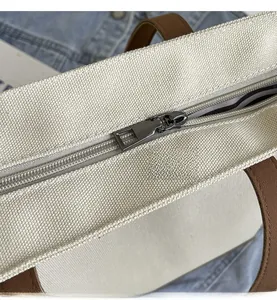 Close-up of smooth metal zipper and brown leather handle on a canvas tote bag