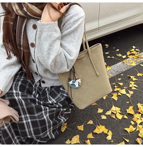 Detailed view of khaki suede tote bag with horse charm on a ginkgo leaf background
