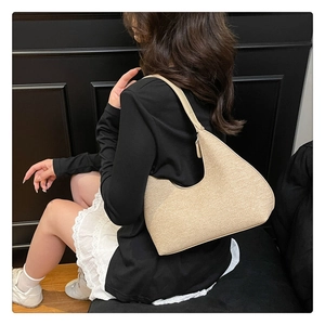 Chic beige textured shoulder bag worn by model against a dark retro backdrop