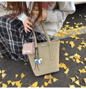 Detail of beige textured bucket bag with blue wooden horse charm on ginkgo leaves