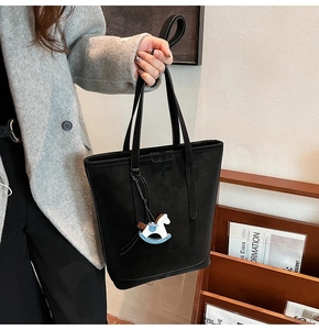Detail of a black suede tote bag with a blue horse charm in a stylish setting