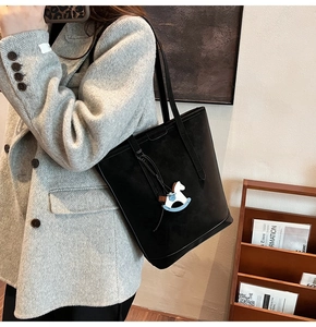 Close-up of a black matte tote bag with a white horse charm on a grey herringbone coat