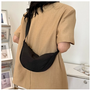 Detail of a black nylon half-moon crossbody bag shown on a person for size reference