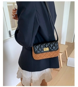 Detail of rhomboid quilted contrast bag with a golden turn-lock on a wooden table