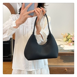 Detail view of a black crescent shoulder bag held by a model in a modern home setting