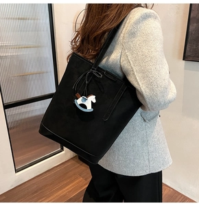 Detail of a black matte leather tote bag featuring a blue and white horse charm
