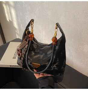 Detail of black glossy hobo bag with gold triangle logo and amber bead handle strap