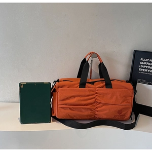Detail of orange nylon travel bag featuring pleated texture and black woven handles