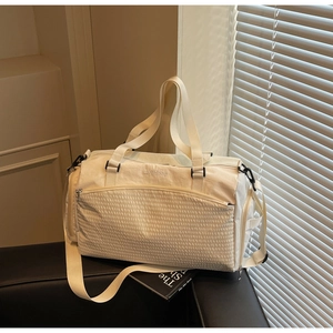 Detail der cremefarbenen Reisetasche mit Wellenstruktur und Stickerei auf Sofa