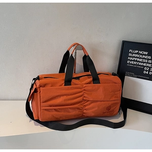 Detail of orange waterproof nylon travel bag featuring a ruched front and logo